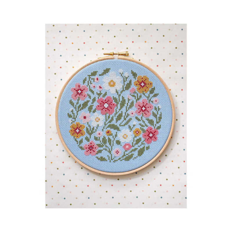 Cross-stitch pattern of a colorful bunch of wildflowers framed in a circular hoop against a multicolor dotted background.