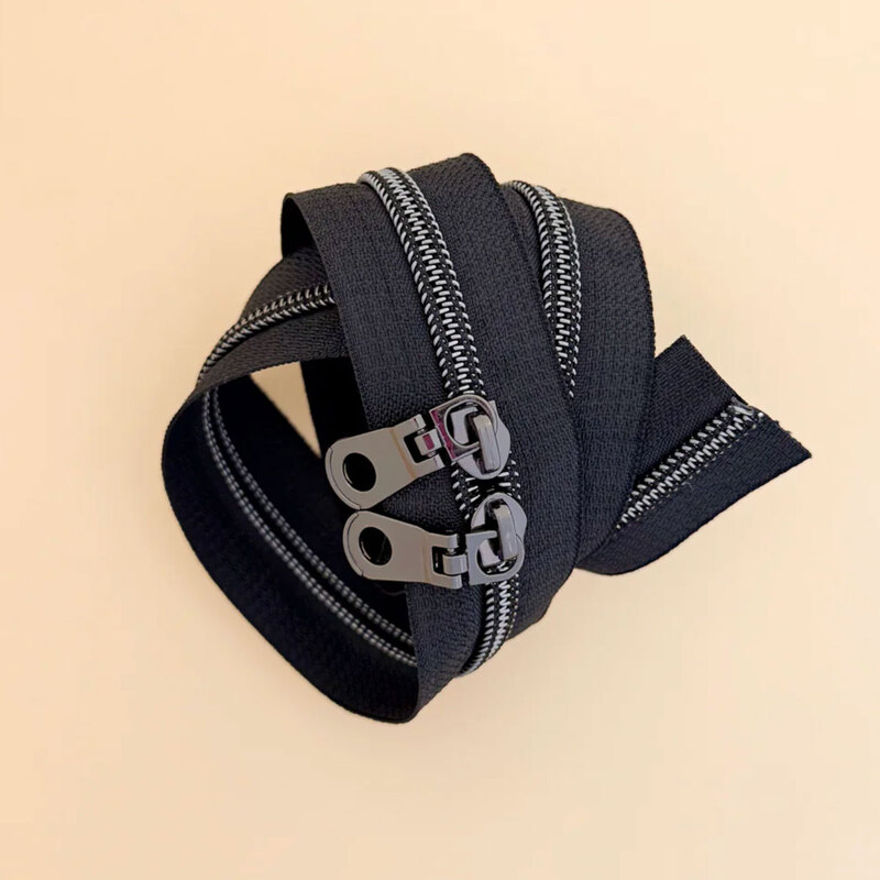 A spool of black zipper tape with black zippers coiled together on a light surface.