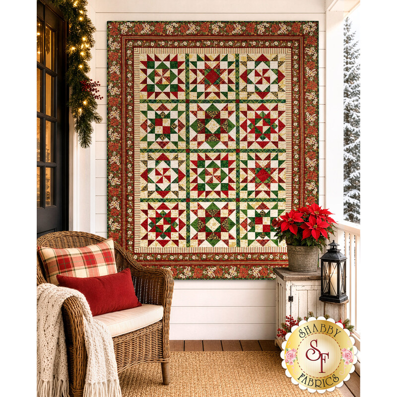 The completed Poinsettias at Christmas Patchwork BOM, colored in cream, green, and red fabrics from the Poinsettias at Christmas collection by Jennifer Bosworth for Riley Blake Designs, hung on a white porch on a snowy day, staged with coordinating décor.