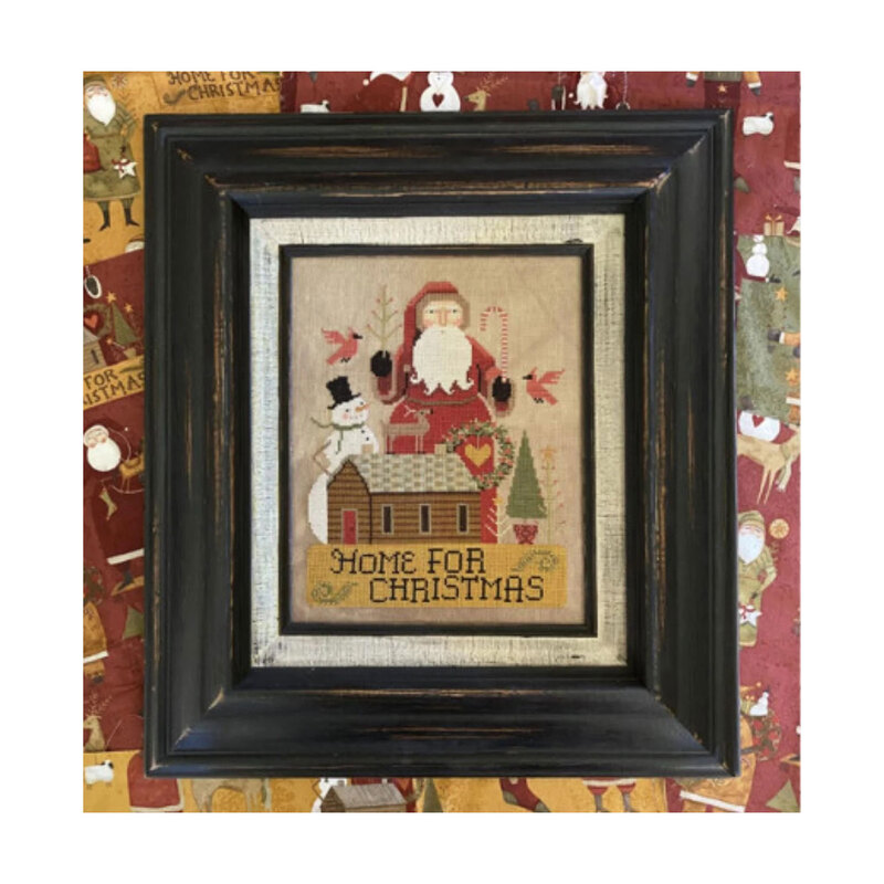 Home for Christmas finished cross stitch pattern in a weathered black frame hung on a Christmas themed wall.