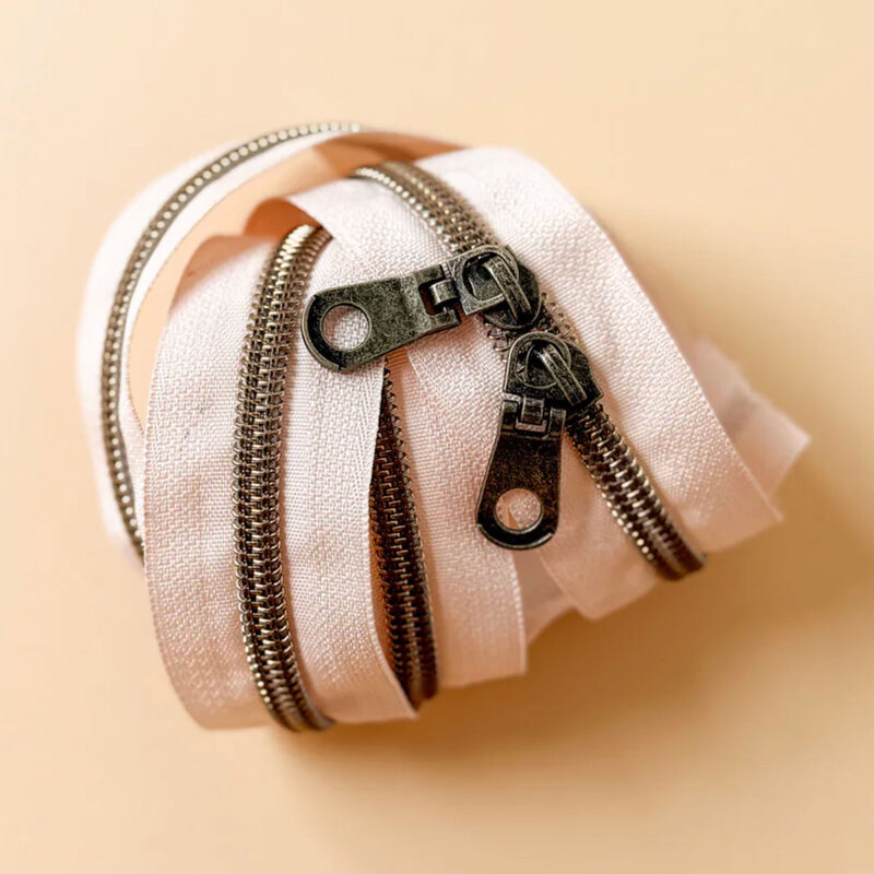 A spool of linen zipper tape with rustic zippers coiled together on a light surface.