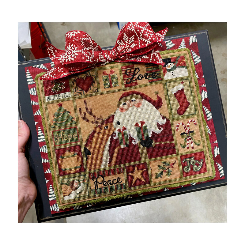 All The Things finished cross stitch pattern in a black frame bordered by a red Christmas border with a red bow on top.