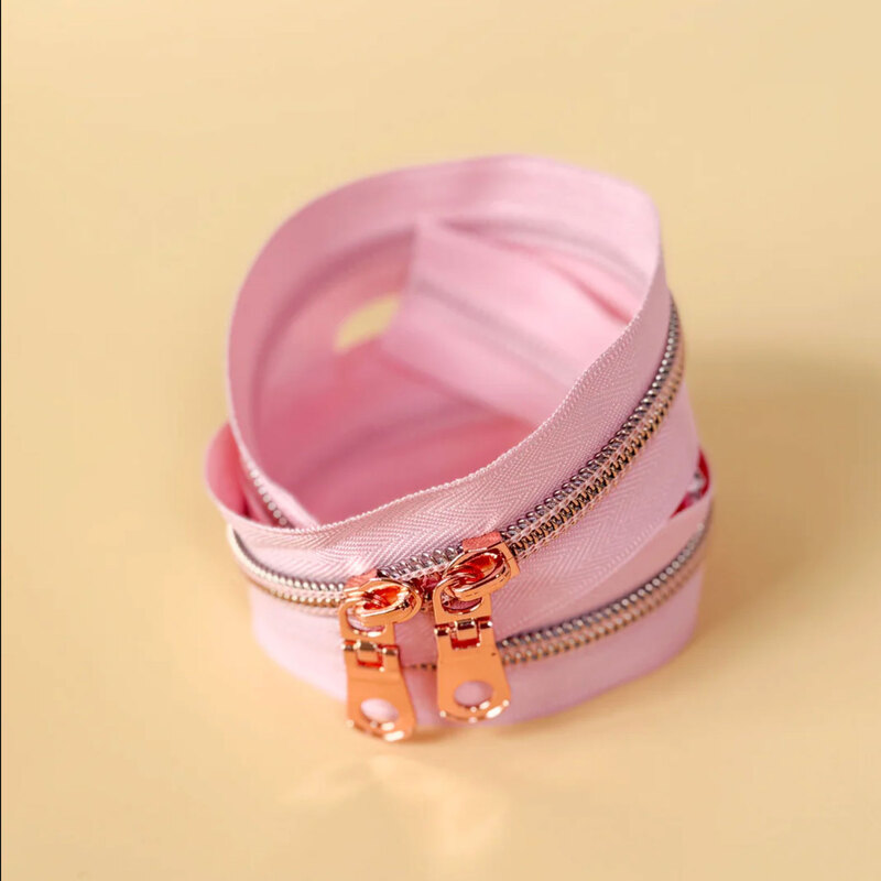 A spool of pink zipper tape with rose gold zippers coiled together on a light surface.