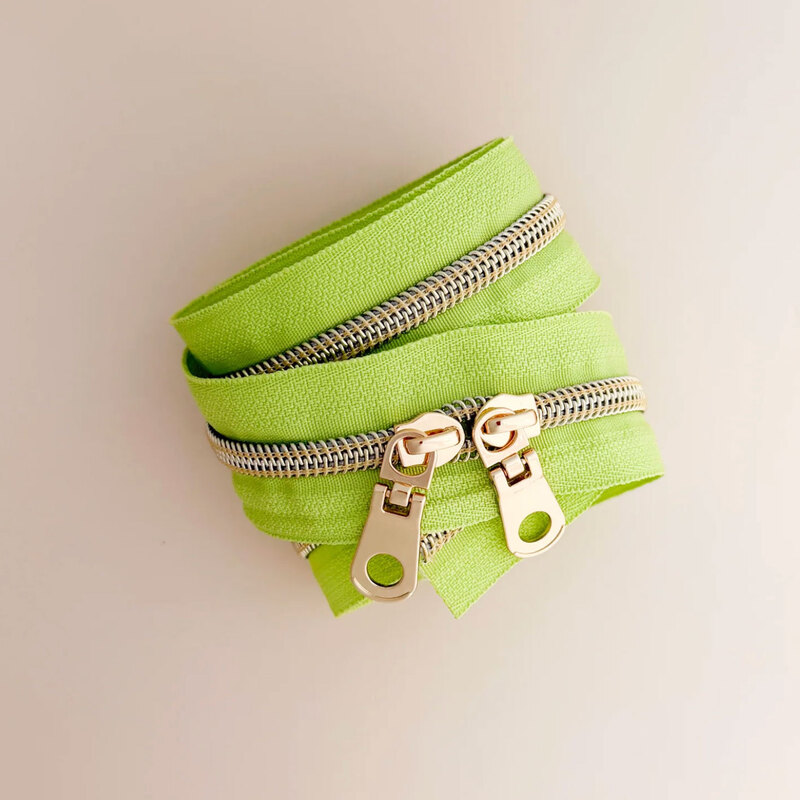 A spool of pesto zipper tape with gold zippers coiled together on a light surface.