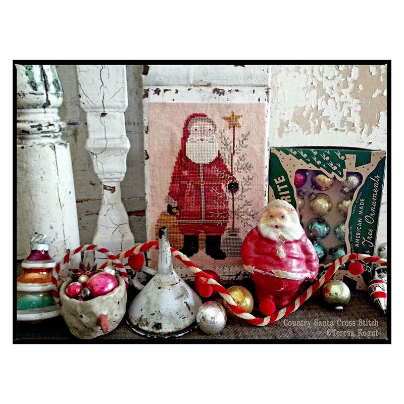 Finished Country Santa cross stitch pattern in a vintage home scene next to porcelain Christmas antiques.