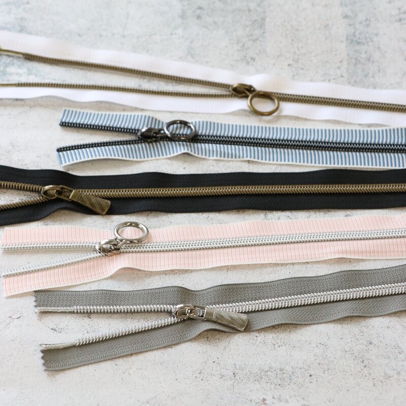 Five zipper pieces in various colors arranged horizontally, showing their coordinating novelty zipper pulls.