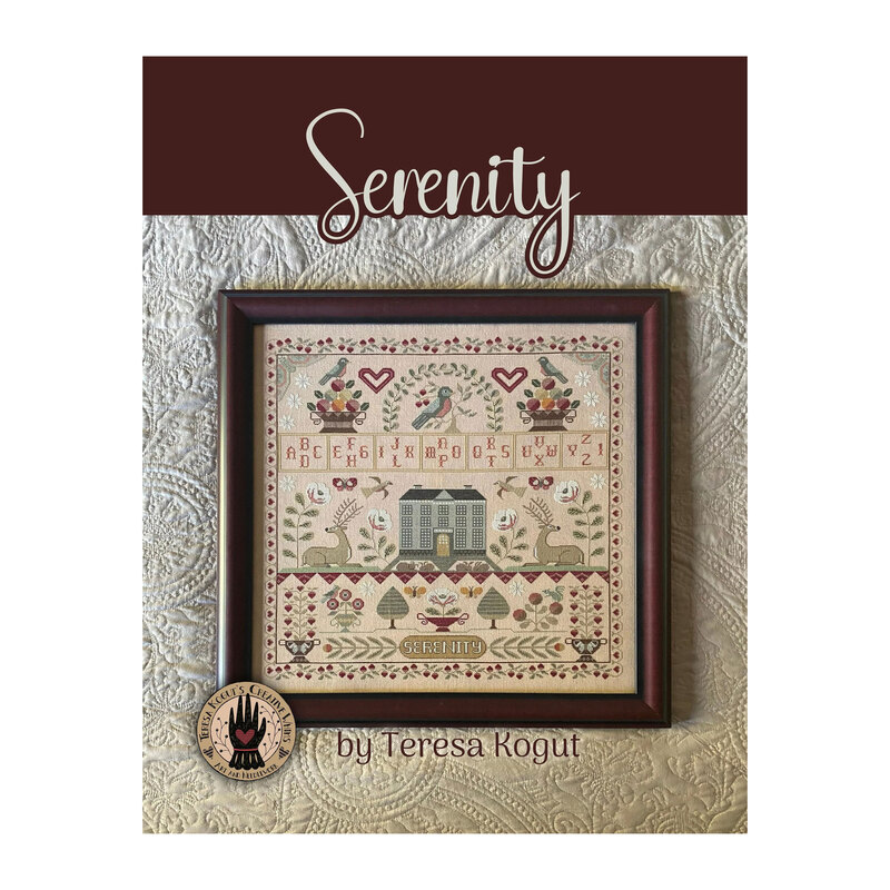 Finished Serenity cross stitch pattern, with an old-timey design of birds, reindeer, fruits, a manor, florals, and a border of berries on a vine all in a wood frame on a cream lace fabric.