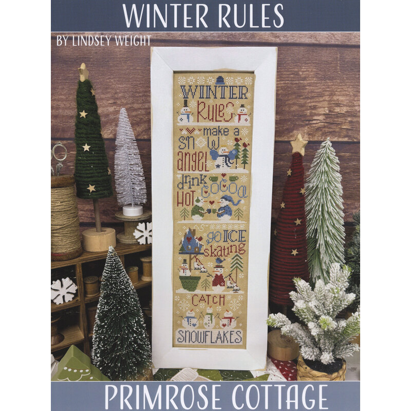 Framed “Winter Rules” cross-stitch pattern displayed among holiday decorations.