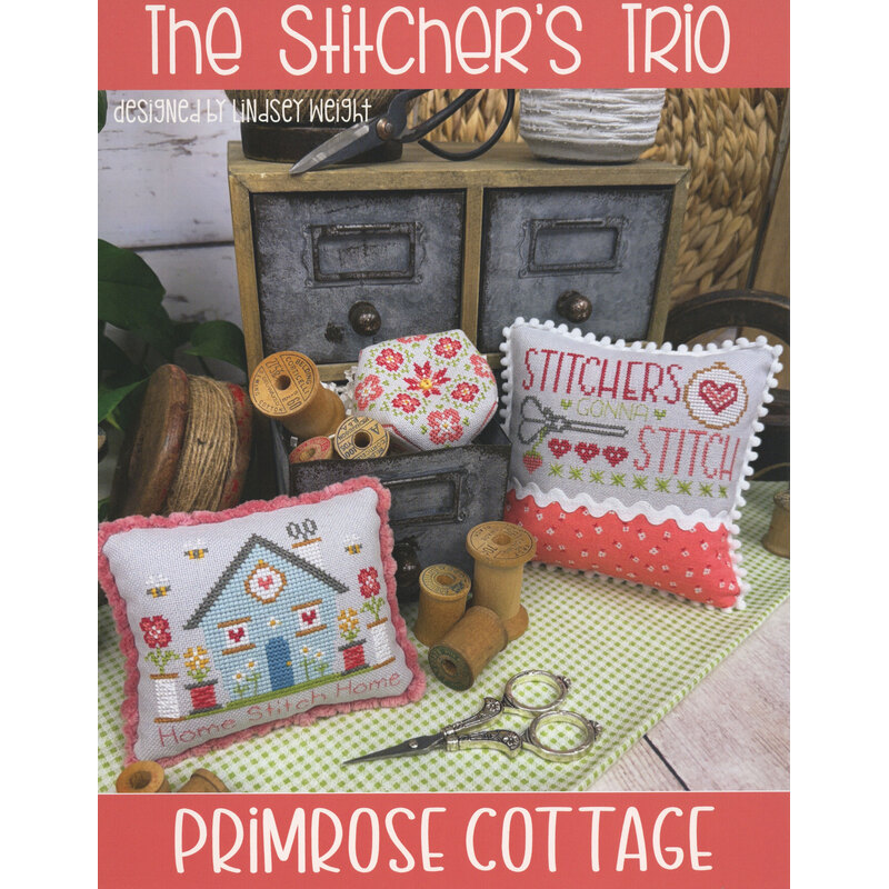 Cross-stitch sampler display with sewing supplies and “Primrose Cottage” title.