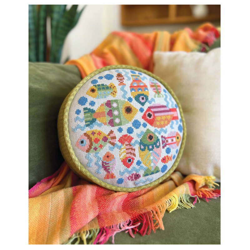 The finished Fish Dish cross stitch project featuring colorful fish, finished as a pillow and staged on a couch with a brightly colored blanket