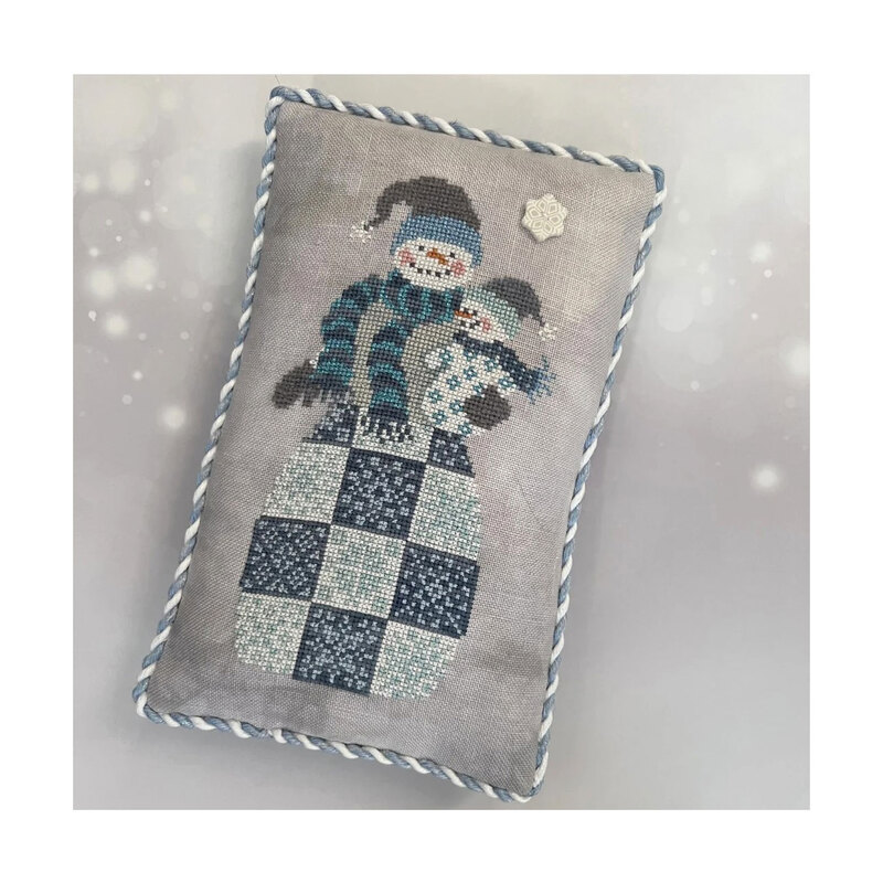 Front cover of the finished Frosty cross stitch pattern displayed on a decorative pillow against a white and gray backdrop.