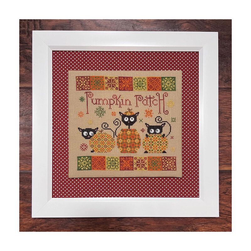 Finished Pumpkin Patch pattern with three black cats playing around pumpkins bordered by a red and white dotted fabric in a white frame.