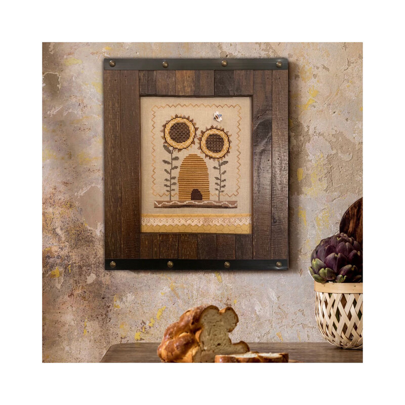 Finished Sunflower Bee cross stitch pattern with sunflowers surrounding a bee hive with a bee flying about in a dark wooden frame.