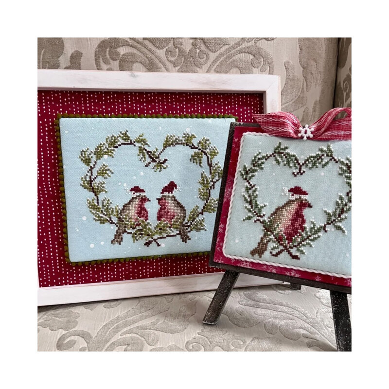 Finished Winter Robin cross stitch patterns in frames on a red fabric.