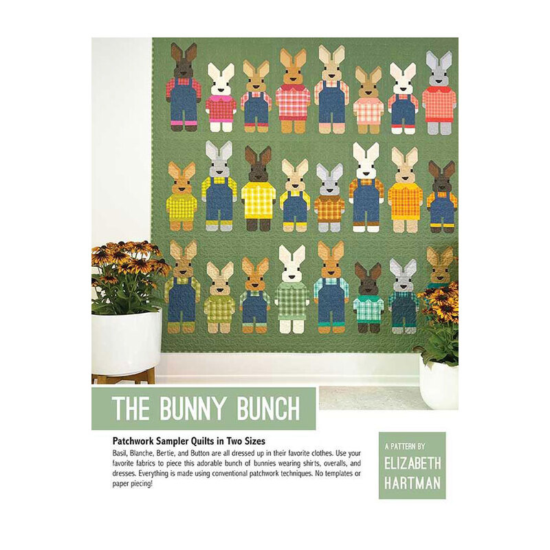 Front cover of the finished The Bunny Bunch sampler quilt with bunnies on a green fabric hung on a white wall with sunflowers on both sides of it.