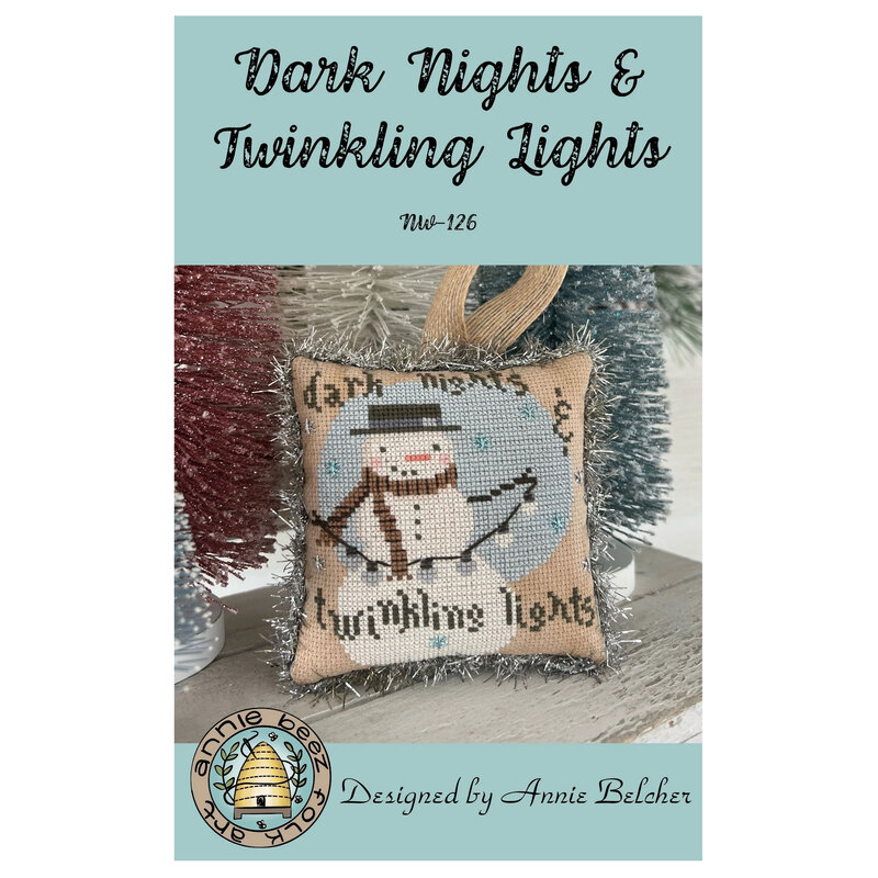 front cover of the Dark Nights & Twinkling Lights pattern featuring the snowman cross stitch finished as a pillow with silver tinsel trim.