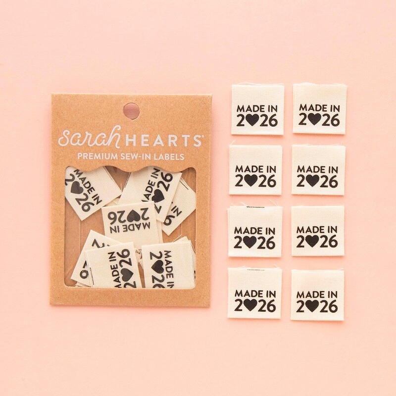 A package of Made in 2026 Sew In Labels next to 8 individual labels on a pink background to show scale and detail.