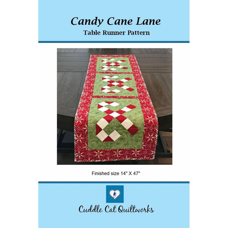 Front cover of the Candy Cane Lane table runner pattern with the runner in green and red hanging off the edge of a wooden table.