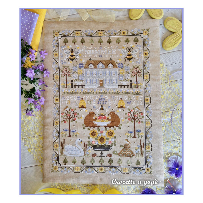 Finished Summer Sampler cross stitch pattern with florals, bees, beehives, trees, and more on a tan linen fabric surrounded by summer florals.