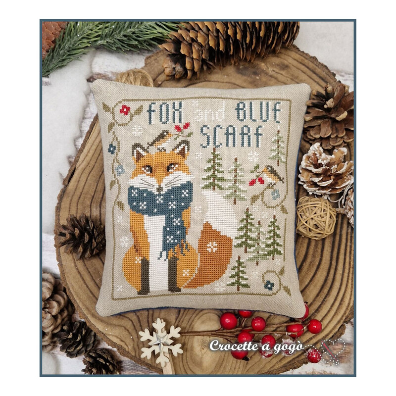 Finished The Little Fox cross stitch pattern on a linen decorative pillow on a wooden stump surrounded by pinecones, berries, and pine needles.