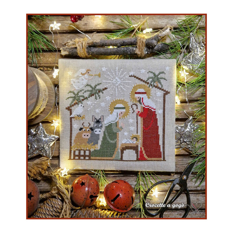 Finished Nativity Collection - 3 cross stitch pattern on a wooden backdrop surrounded by twigs, pine needles, stars, lights, pinecones, and bells.