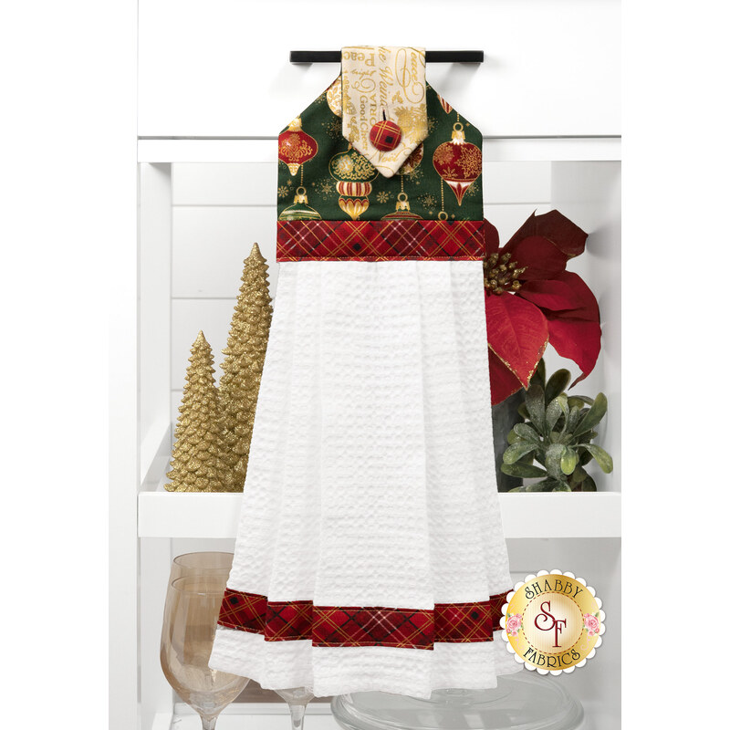 The completed Hanging Towel colored in red, green, black, and cream fabrics from the Poinsettias at Christmas collection by Jennifer Bosworth for Riley Blake Designs, staged on a kitchen drawer with coordinating decor.