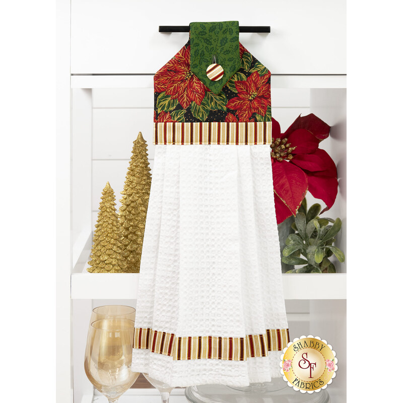 The completed Hanging Towel colored in red, green, black, and cream fabrics from the Poinsettias at Christmas collection by Jennifer Bosworth for Riley Blake Designs, staged on a kitchen drawer with coordinating decor.