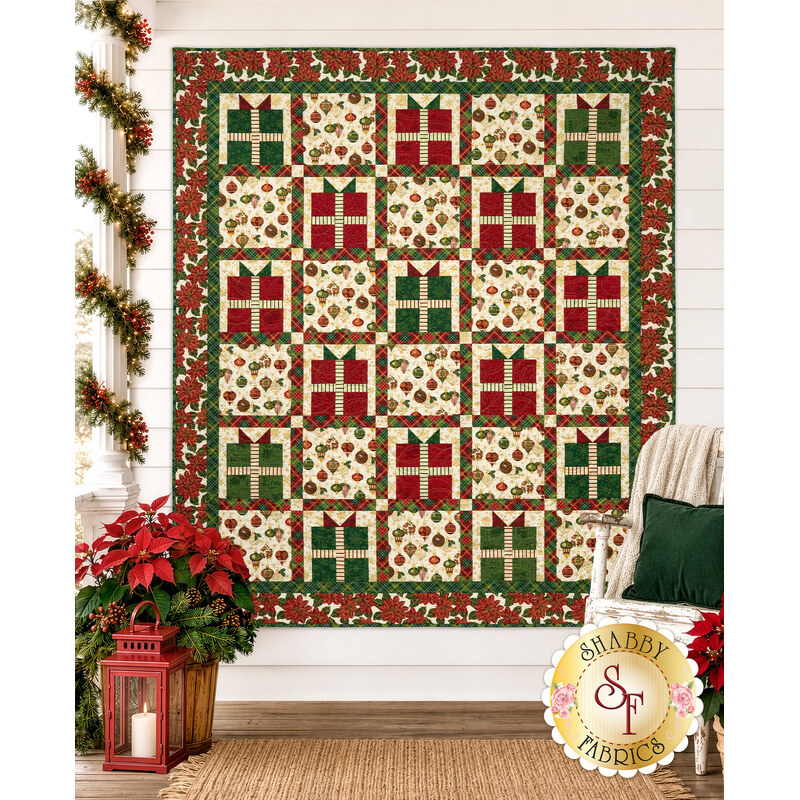 The completed A Gift for You Quilt, colored in red, green, and white, and gold metallic fabrics from the Poinsettias at Christmas collection by Jennifer Bosworth for Riley Blake Designs, staged on a white shiplap wall with coordinating furniture and décor.