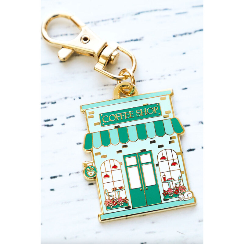Gold keychain charm shaped like a coffee shop.