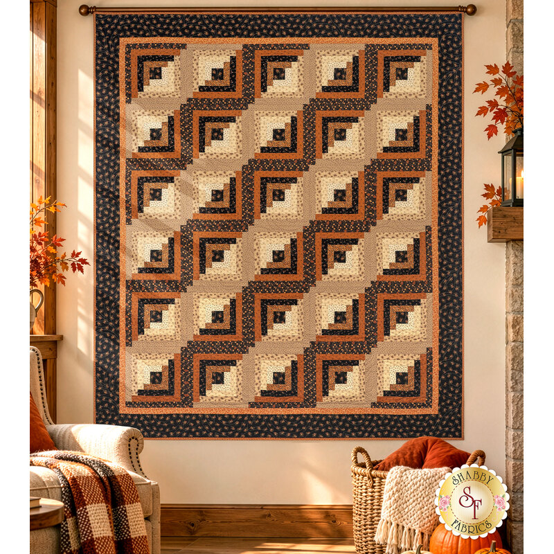The completed Log Cabin Throw Quilt, colored in black, brown, tan, orange, and cream fabrics from the Midnight Cheddar collection from Marcus Fabrics, hung on a sunlit living room wall and staged with coordinating furniture.