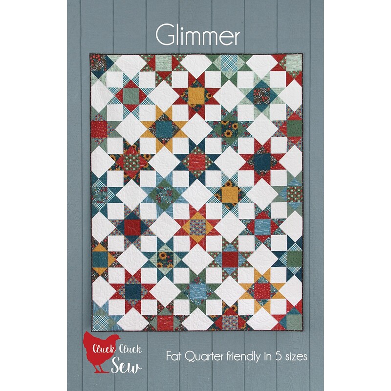 The front of the Glimmer pattern with the completed quilt hung up on a blue wooden wall.