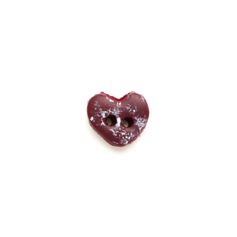 Red heart-shaped button with two holes and a white speckled finish on a white background.
