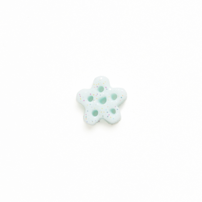 Small bluish white clay snowflake button with speckles of glitter on a white background.