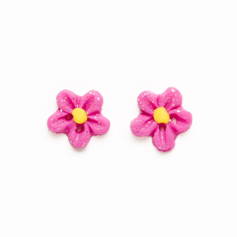 Two pink glittery flower-shaped clay buttons with yellow centers on a white background.