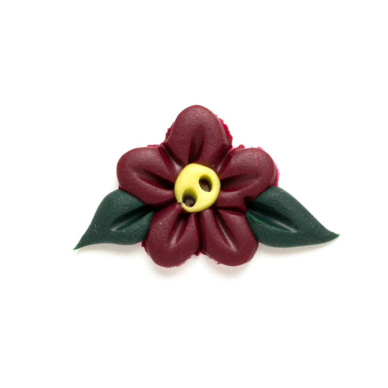 Red, yellow, and dark green clay poinsettia button isolated on a white background.