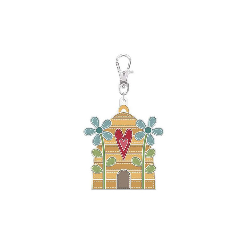 Enamel pin with a clip holding a beehive with a red and pink heart on it next to two blue flowers isolated on a white background.