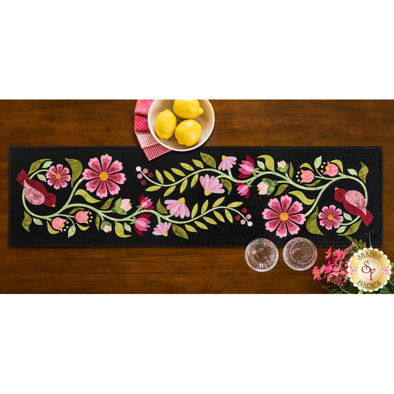 The completed Baltimore Garden Table Runner in Rose, staged on a wooden table with four black chairs and a bowl of lemons.
