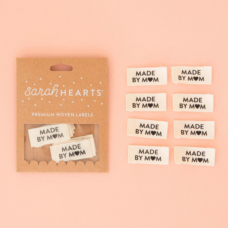 A package of Made by mom Sew In Labels next to 8 individual labels on a pink background to show scale and detail.