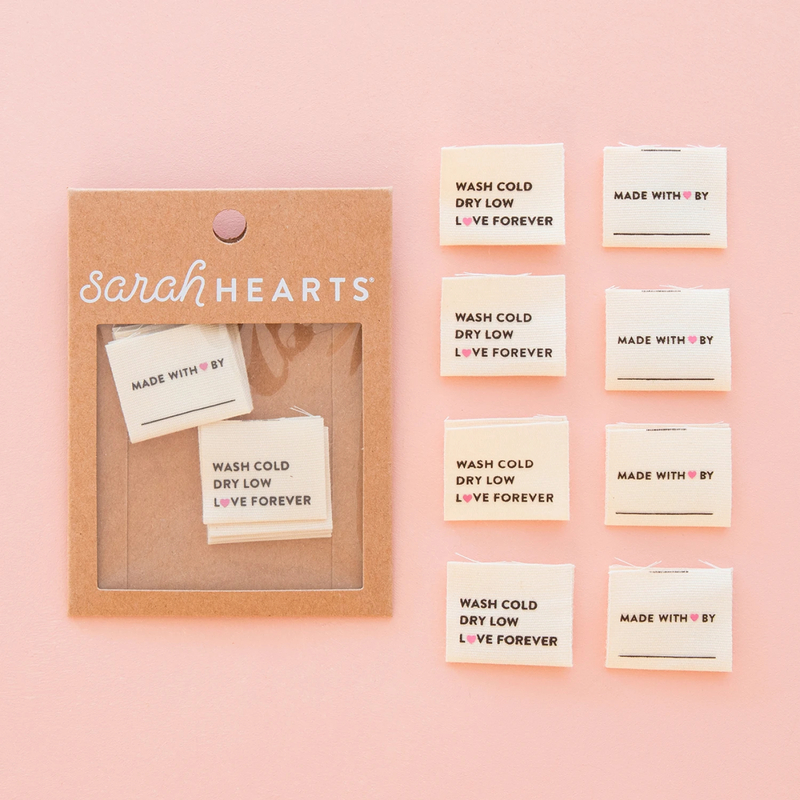 A package of wash cold, dry low, love forever labels next to 8 individual labels on a pink background to show scale and detail.