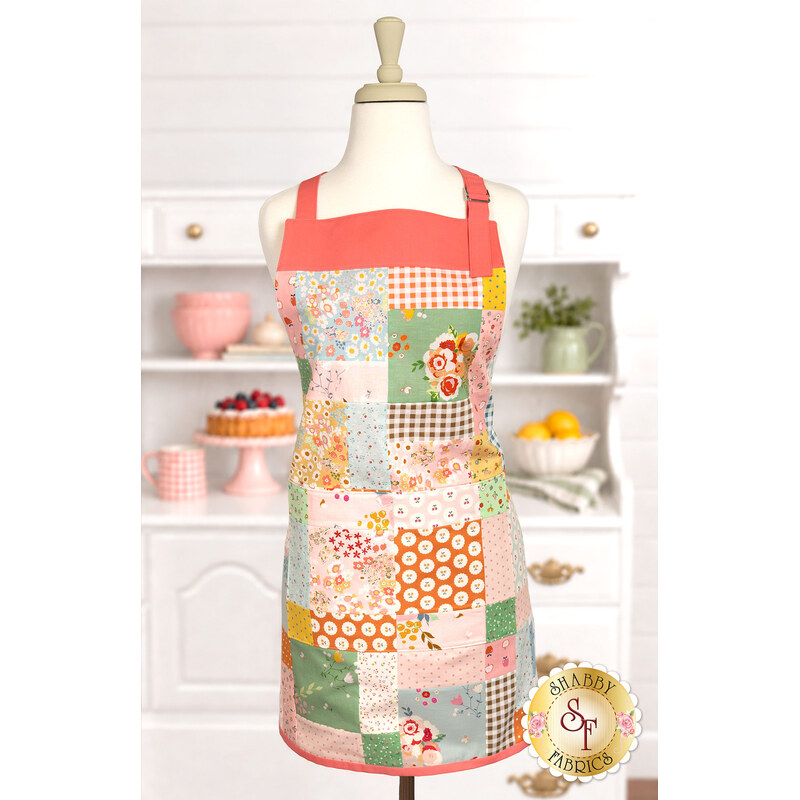 The completed Simply Charming Apron colored in bright 30s style fabrics from the Cotton Nook collection by Riley Blake Designs, displayed on a mannequin with colorful coordinating décor in the background. 