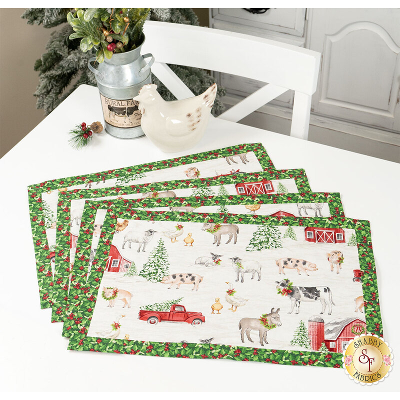 The four completed Self-Binding Placemats, fanned out and colored in red, green, and white fabrics from the Barnyard Christmas collection by Northcott Fabrics, staged on a white table with coordinating décor.