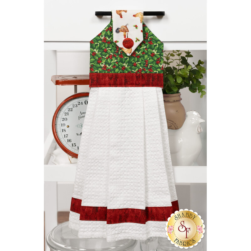 The completed Hanging Towel colored in red, green, and white fabrics from the Barnyard Christmas collection by Northcott Fabrics, staged on a kitchen drawer with coordinating decor.