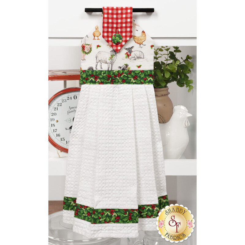 The completed Hanging Towel colored in red, green, and white fabrics from the Barnyard Christmas collection by Northcott Fabrics, staged on a kitchen drawer with coordinating decor.