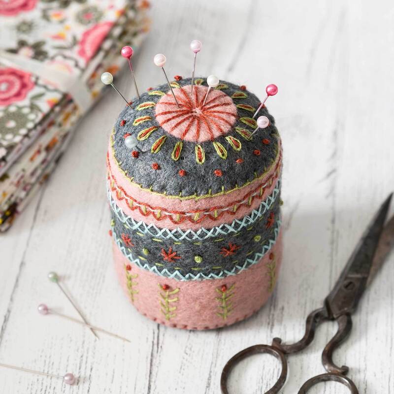 The completed Felt Wool Mix pincushion staged with pins, fabric, and a rustic pair of scissors.