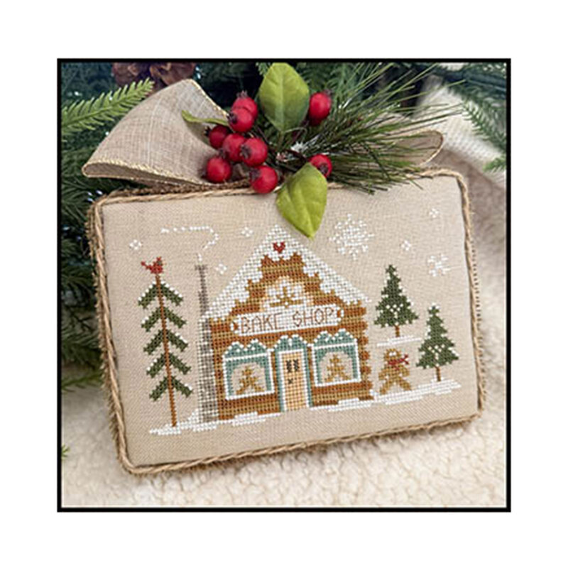 Cross stitched bakery shop project with berries, pine branches, and a decorative bow.