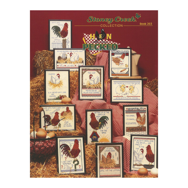 Front cover of the Hen Pecked cross stitch book with all of the finished designs in black frames lying on hay bales and a red picnic blanket.