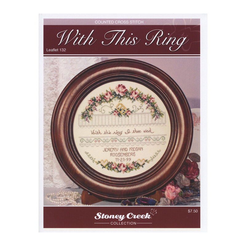 Front cover of the With This Ring cross stitch pattern with the finished design in a wooden circle frame in front of a lace fabric.