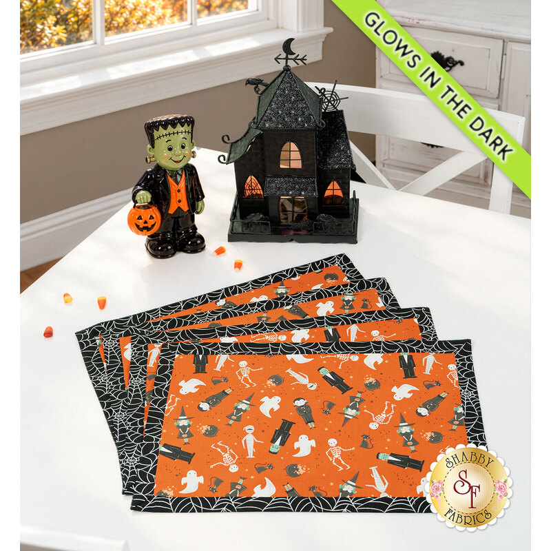 The four completed Self-Binding Placemats, fanned out and colored in gray, mint green, white, pink, and orange fabrics from the Frank and Friends collection by Riley Blake Designs, staged on a white table with coordinating Halloween décor.
