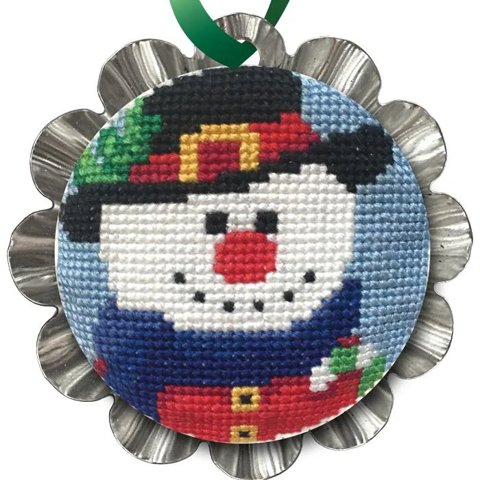 Jolly Snowman Tin Kit featuring a cross stitched snowman in a black hat with colorful winter details, framed in a silver tart tin with a green hanging ribbon.