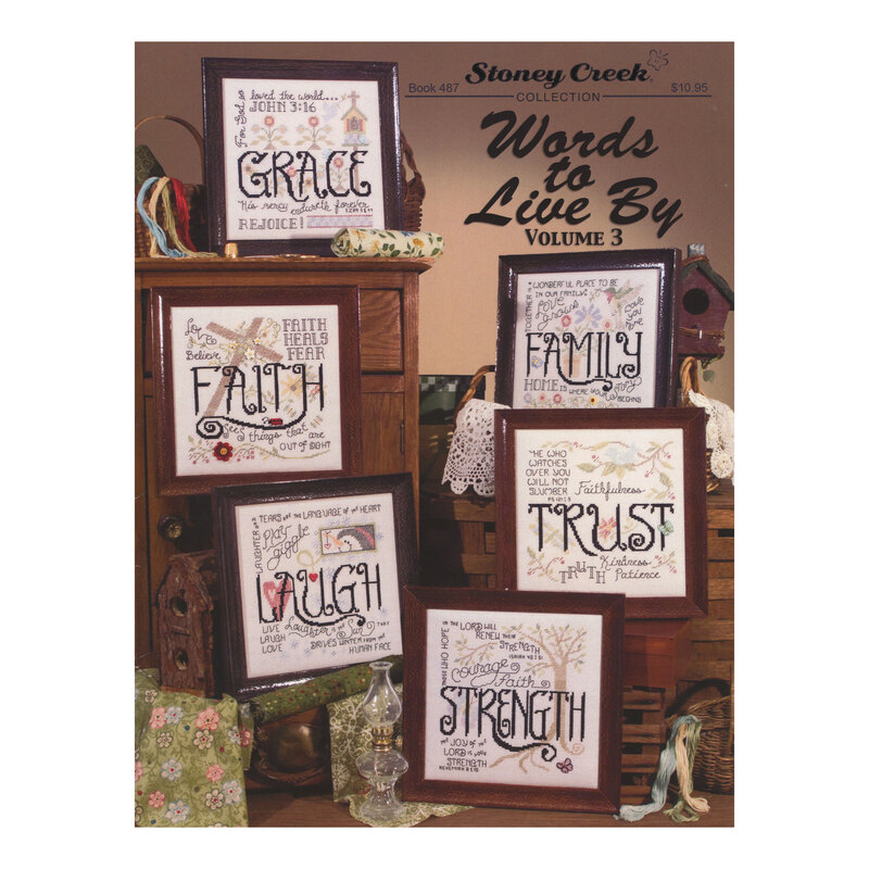 Front cover of the Words to Live By Volume 3 cross stitch pattern book with the six finished patterns in wooden frames propped in a quaint house scene.